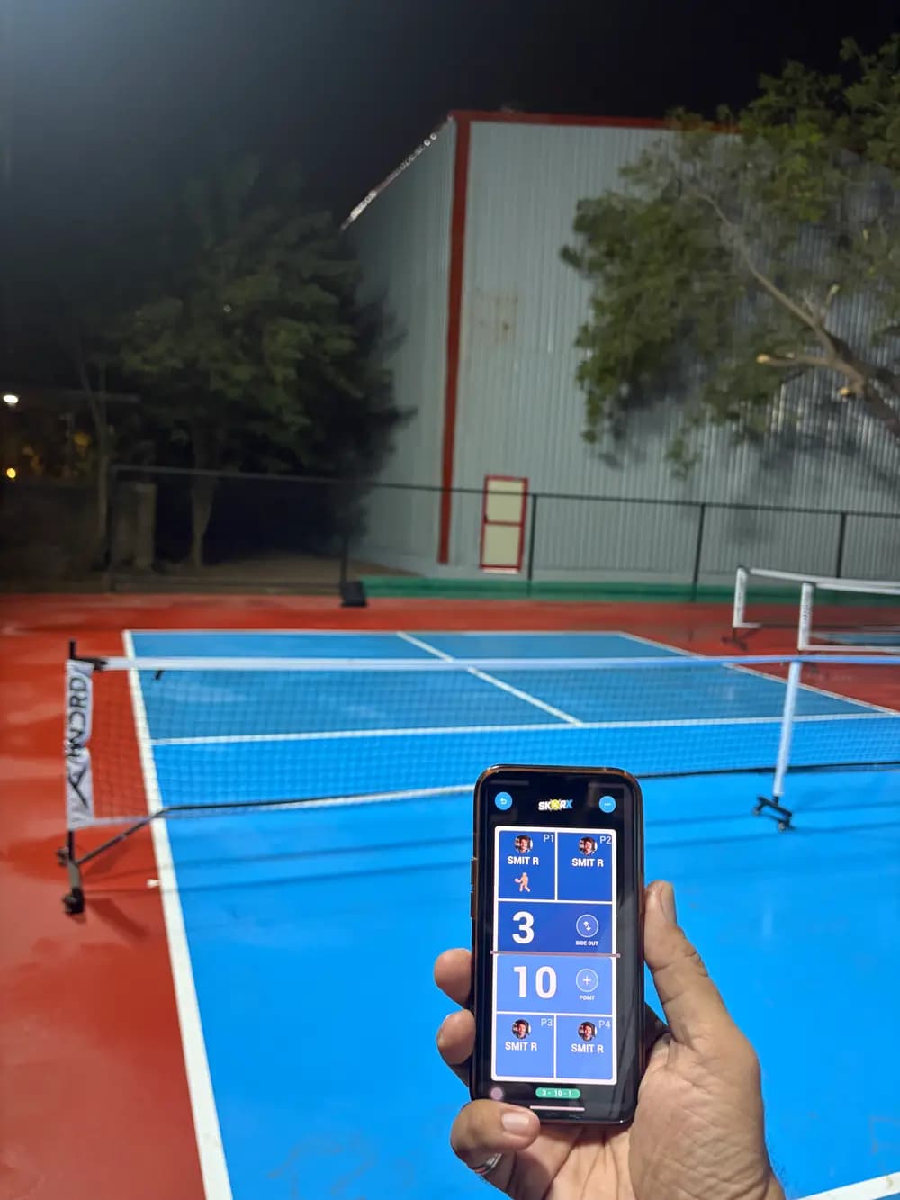 SkorX live score on a phone at an outdoor court