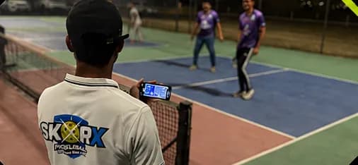 Scorer keeping a live score on a phone beside a night doubles match
